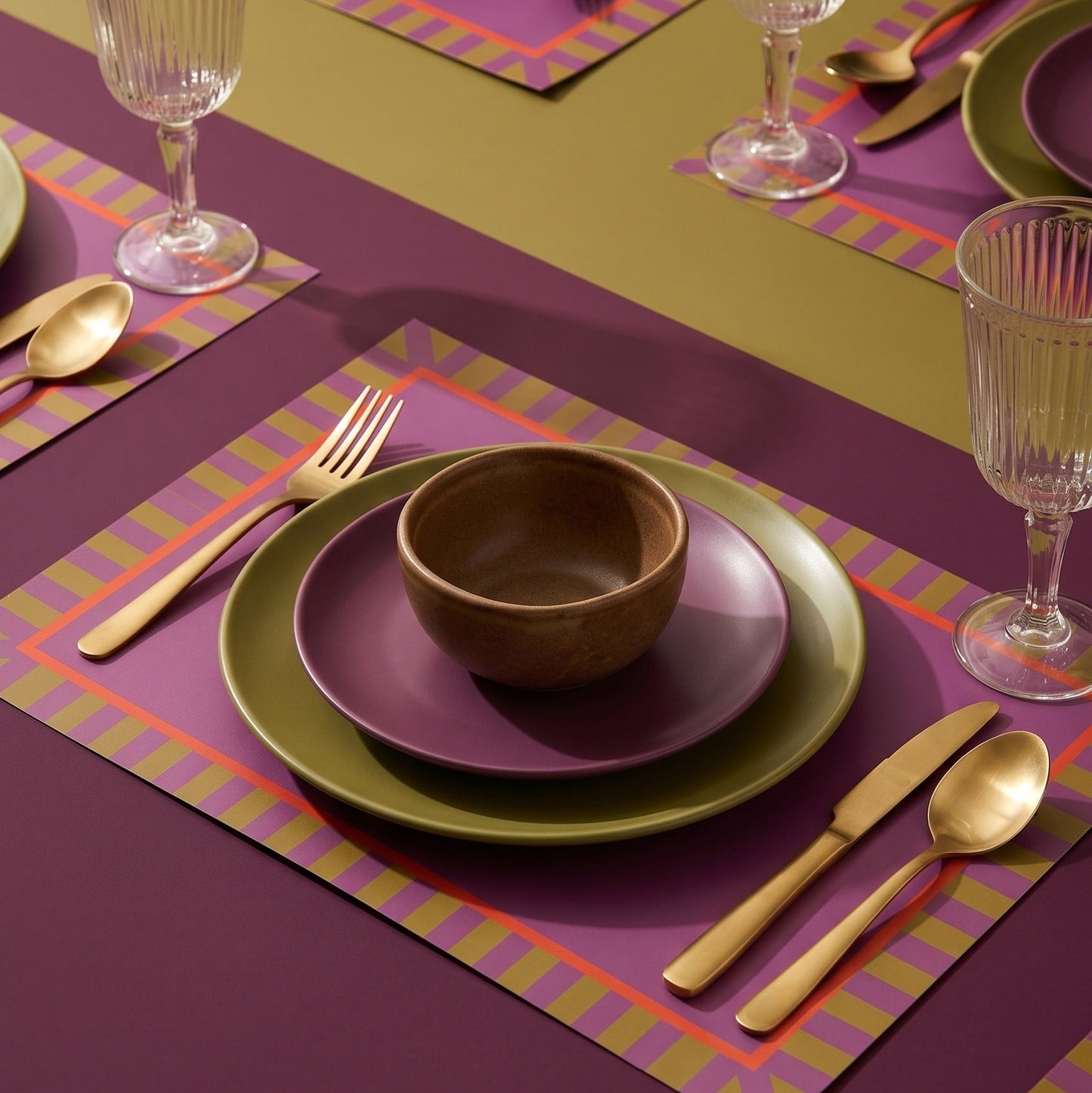 Dining table setting with green plates, brown bowl, and gold cutlery on a purple placemat.