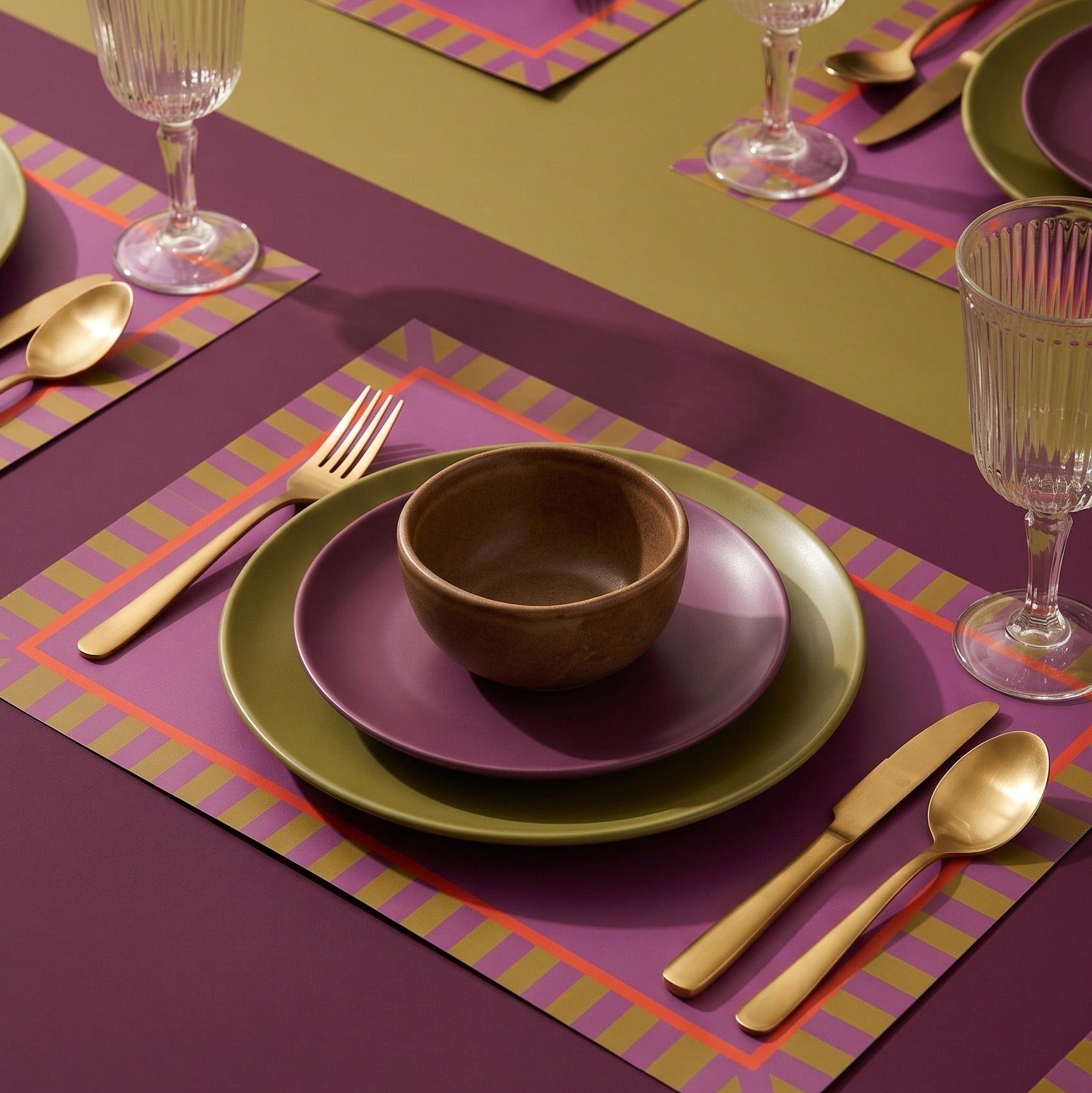 Dining table setting with green plates, brown bowl, and gold cutlery on a purple placemat.