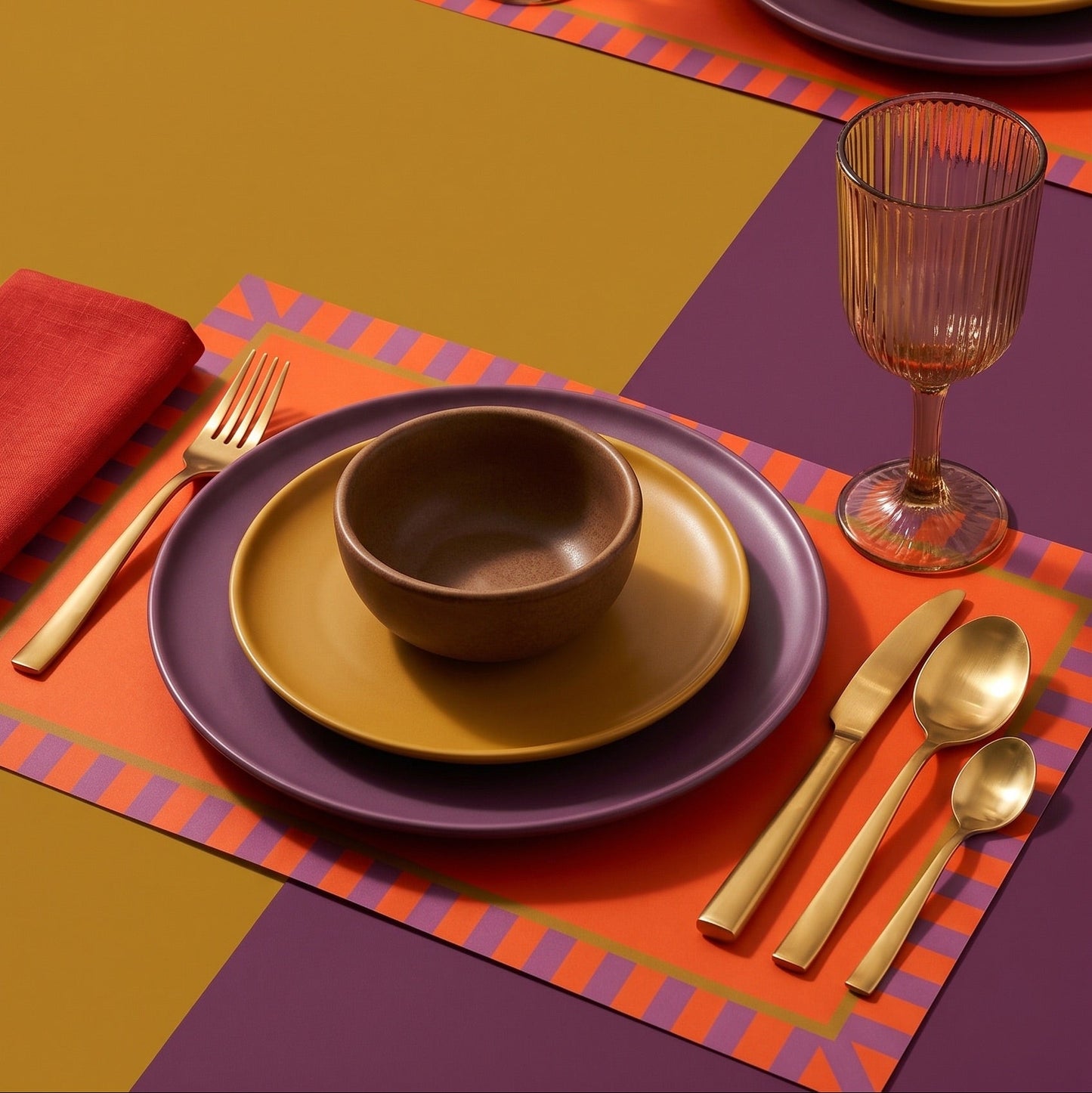Colorful table setting with plates, bowl, cutlery, and glass on a geometric placemat.
