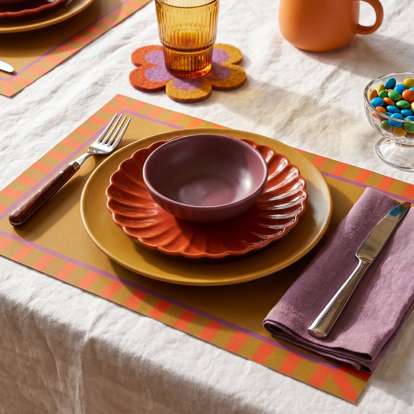 Colorful table setting with plates, bowls, and cutlery on a placemat.