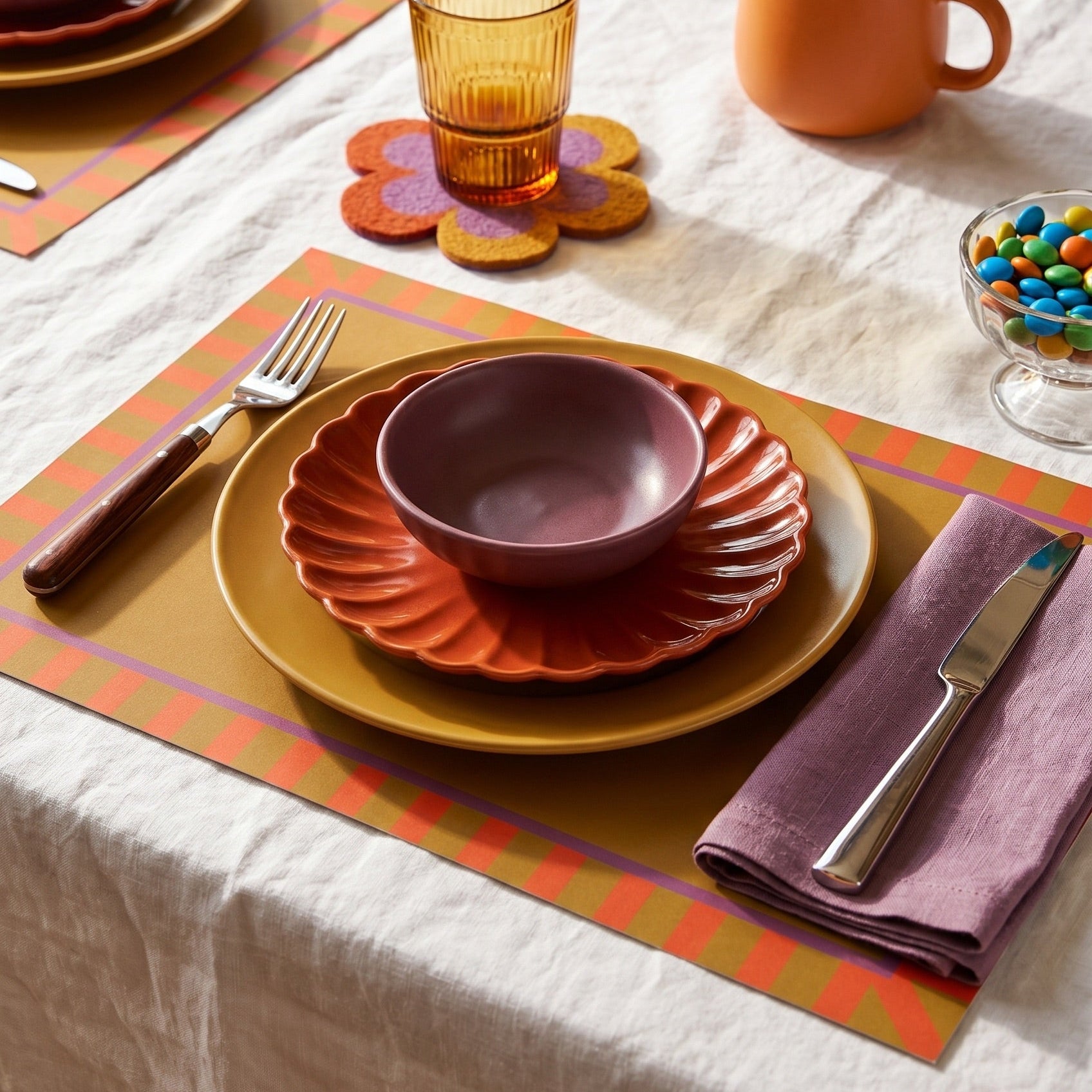 Colorful table setting with plates, bowls, and cutlery on a placemat.