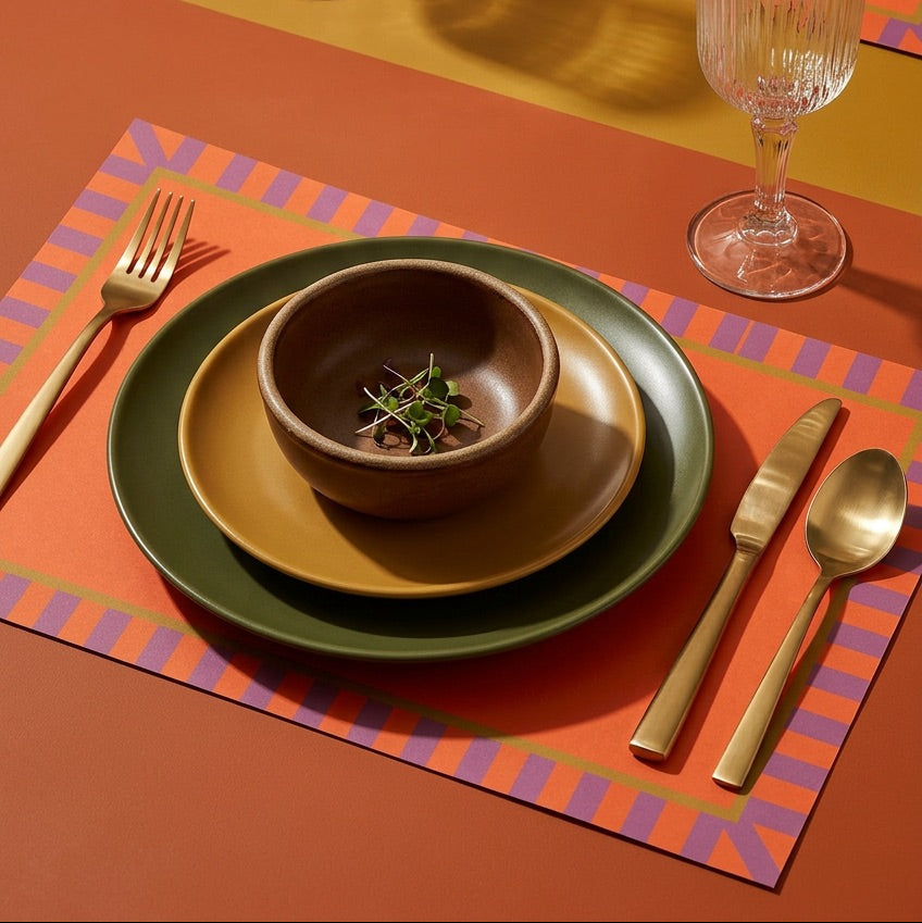 Dinner setting with plates, bowl, cutlery, and a glass on a colorful placemat.