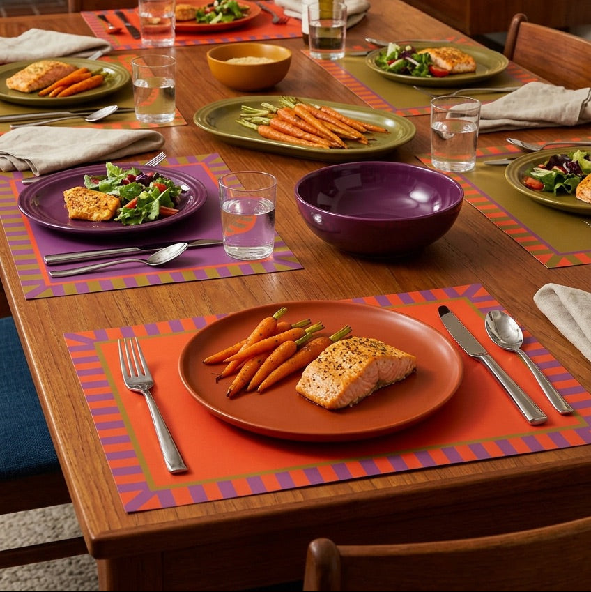 Dining table set with plates of food, including salmon and carrots, on colorful placemats.
