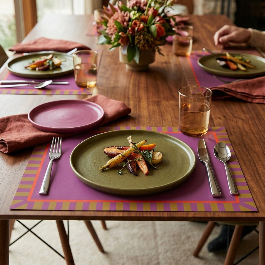 Dining table set with plates, glasses, and cutlery on a purple paper placemat.