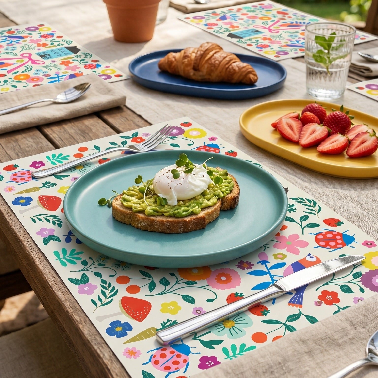 Colorful floral paper placemats styled on an outdoor patio table with avocado toast and fresh fruit