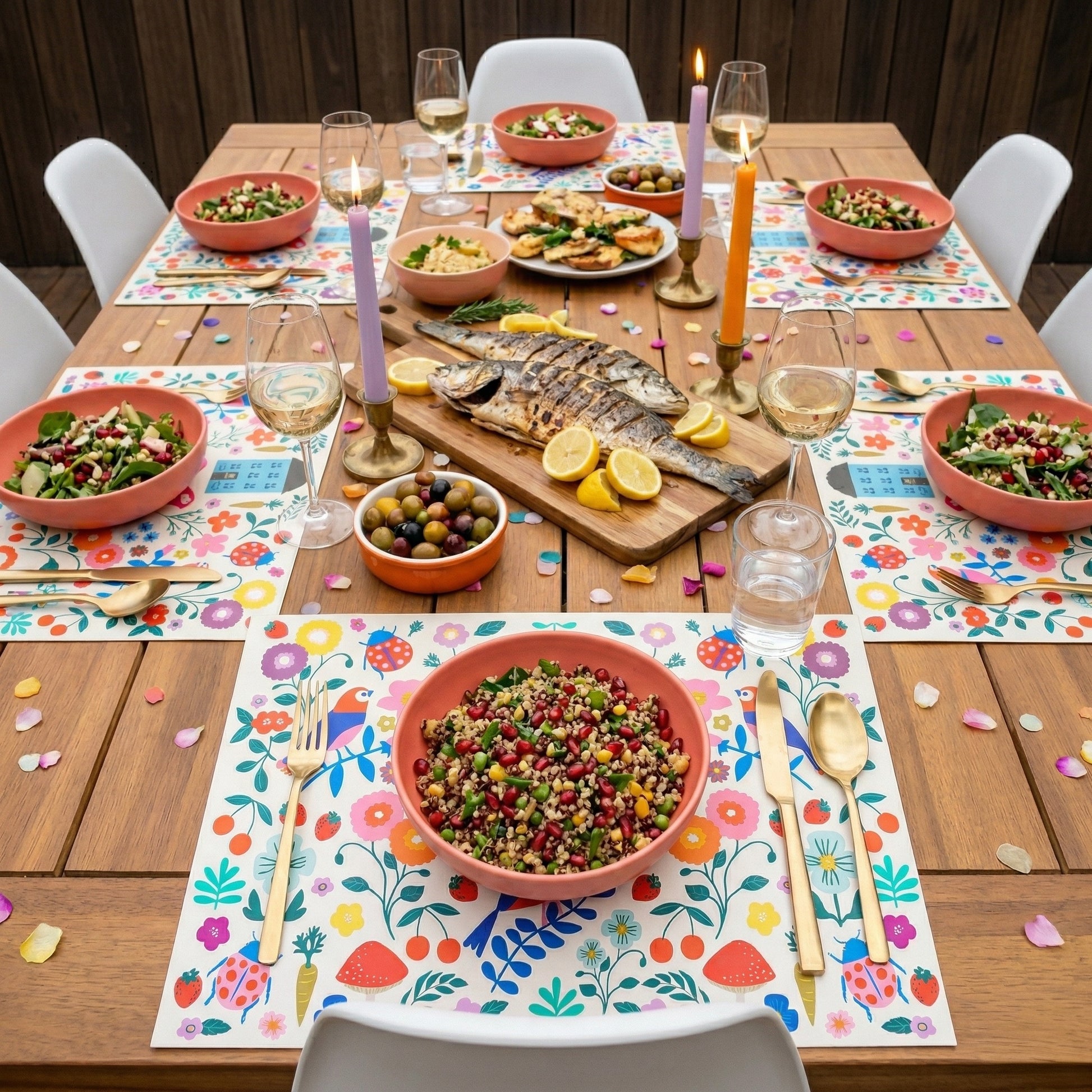 Colorful floral paper placemats styled on an outdoor patio table with fish and salads.