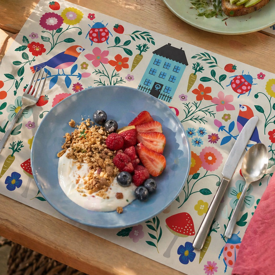 Colorful floral paper placemats styled on an outdoor patio table with avocado toast, pancakes, and fresh fruit