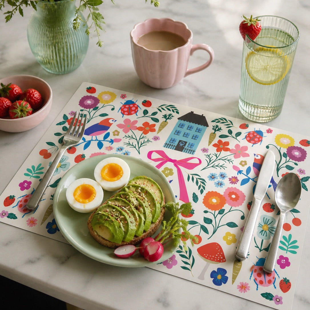 Colorful floral paper placemats styled on a marble table with avocado toast, eggs, and fresh fruit