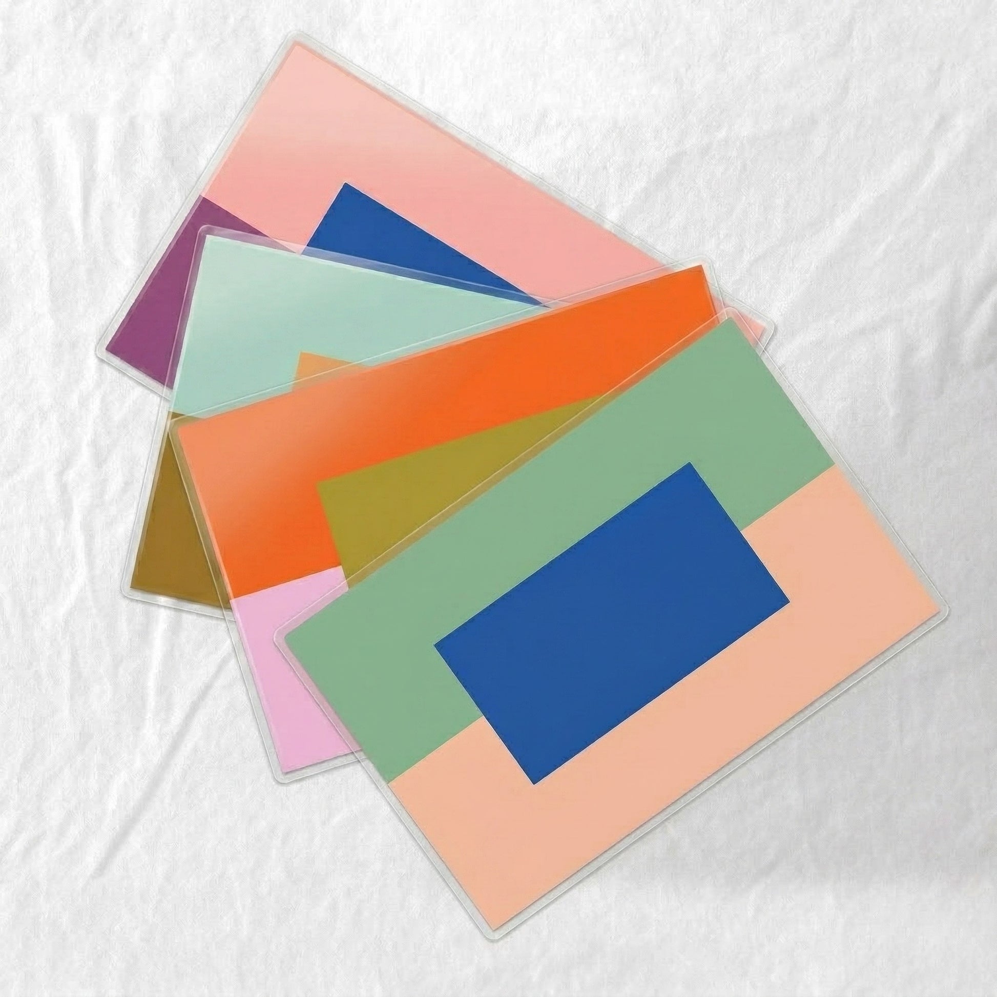 Colorful laminated paper placemats stacked on a textured white surface