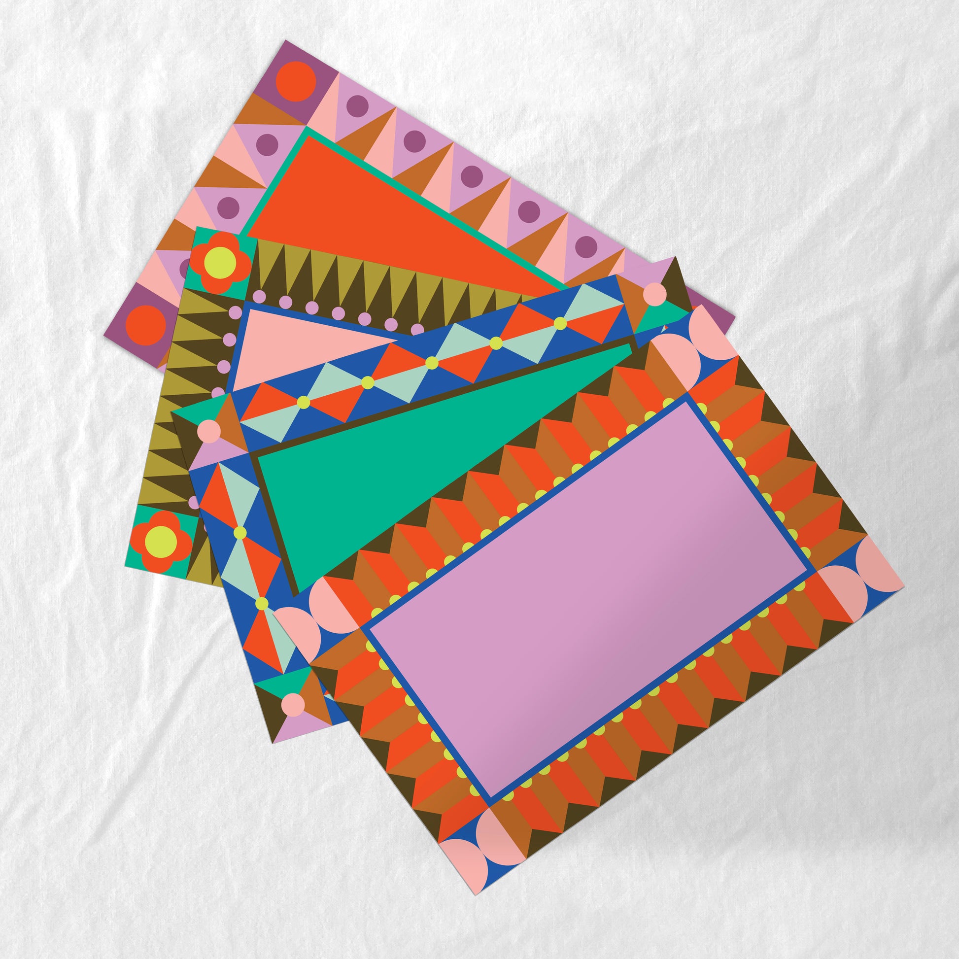 Set of 4 colorful geometric patterned paper placemats on a white background