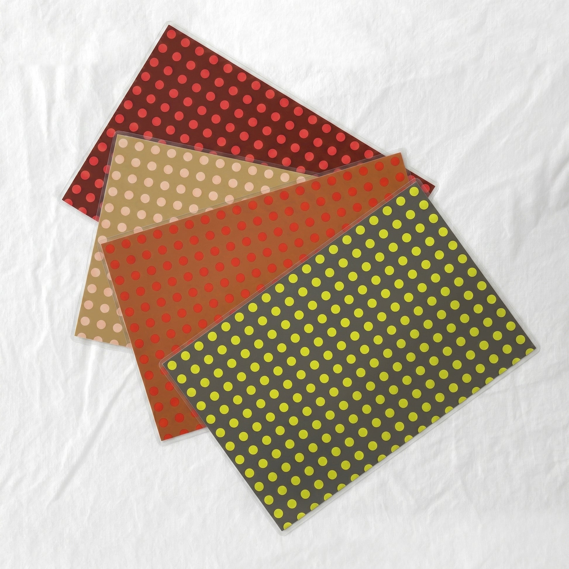 Four sheets of laminated paper placemats with polka dot patterns on a white background