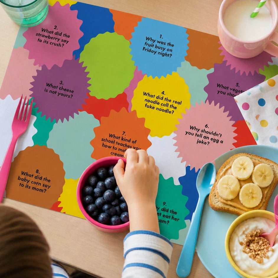 Child playing with a colorful paper placemat at a table with food and drinks.