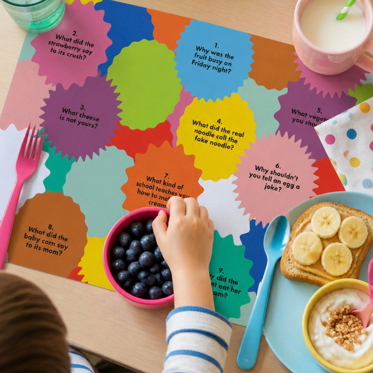 Child playing with a colorful paper placemat at a table with food and drinks.