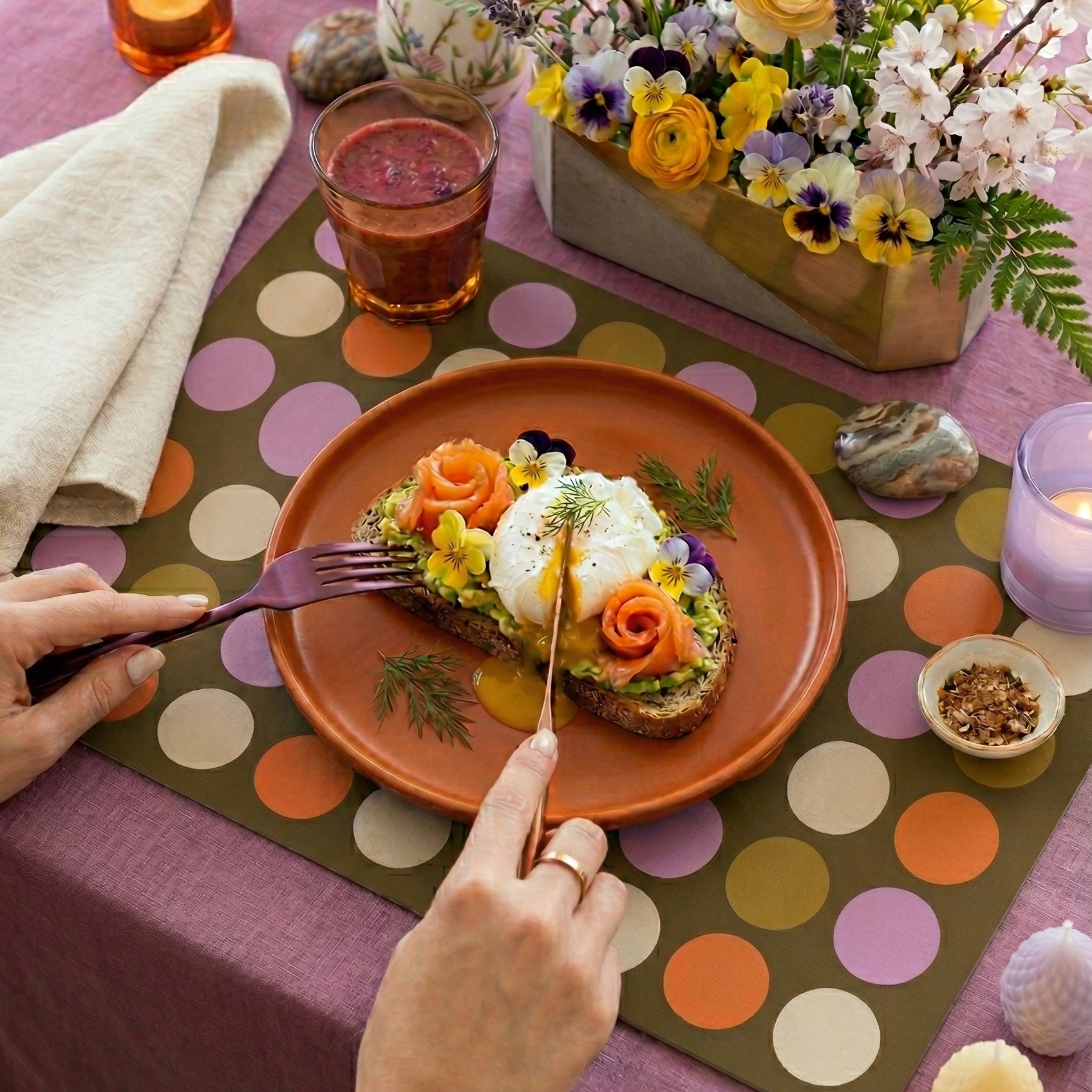Table setting with a colorful polka dot paper placemat, floral arrangement, and a dish of food.