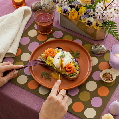 Table setting with a colorful polka dot paper placemat, floral arrangement, and a dish of food.