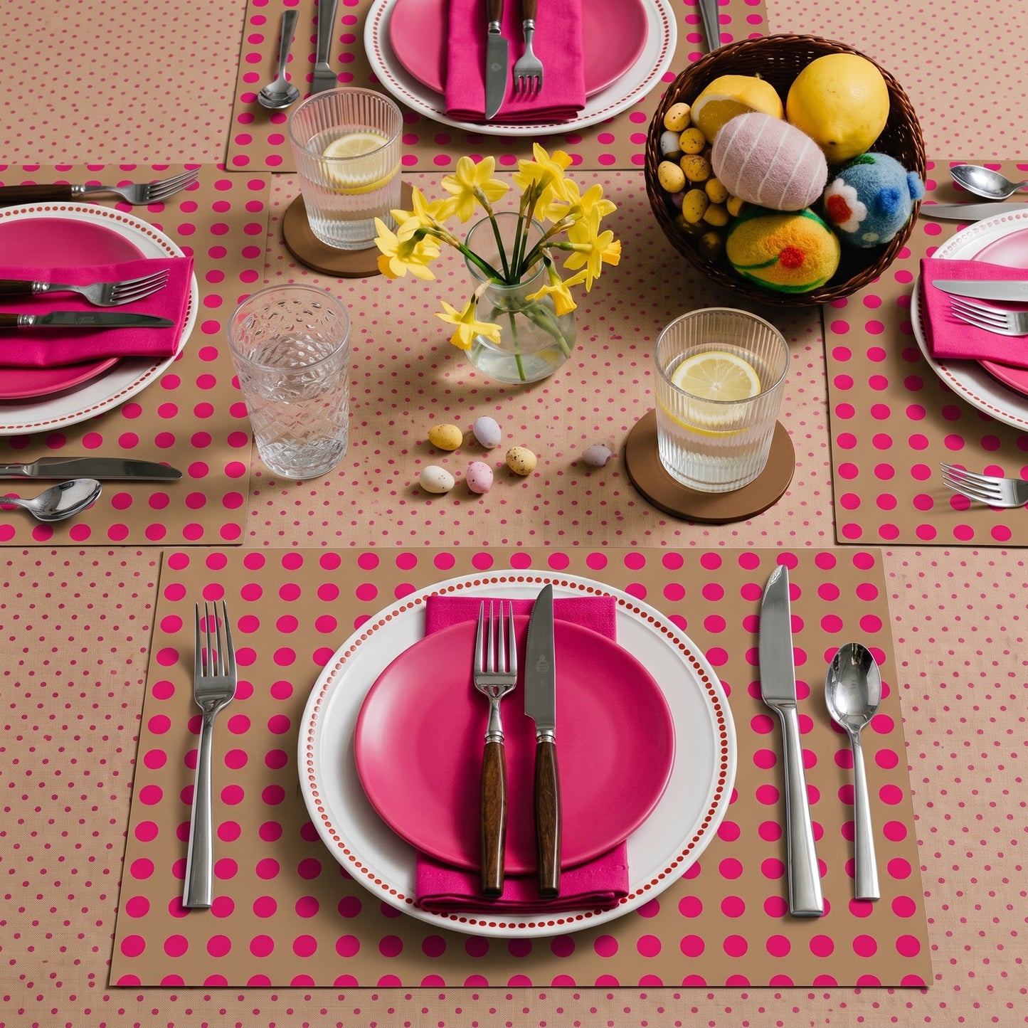 Dining table setting with pink plates, napkins, and cutlery on a polka dot paper placemat.