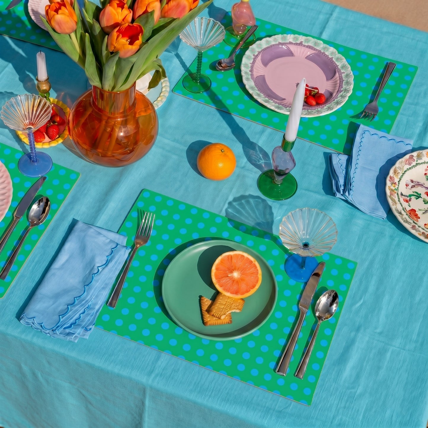 Colorful table setting with plates, cutlery, and a vase of flowers on a green and blue polka dot paper placemat.