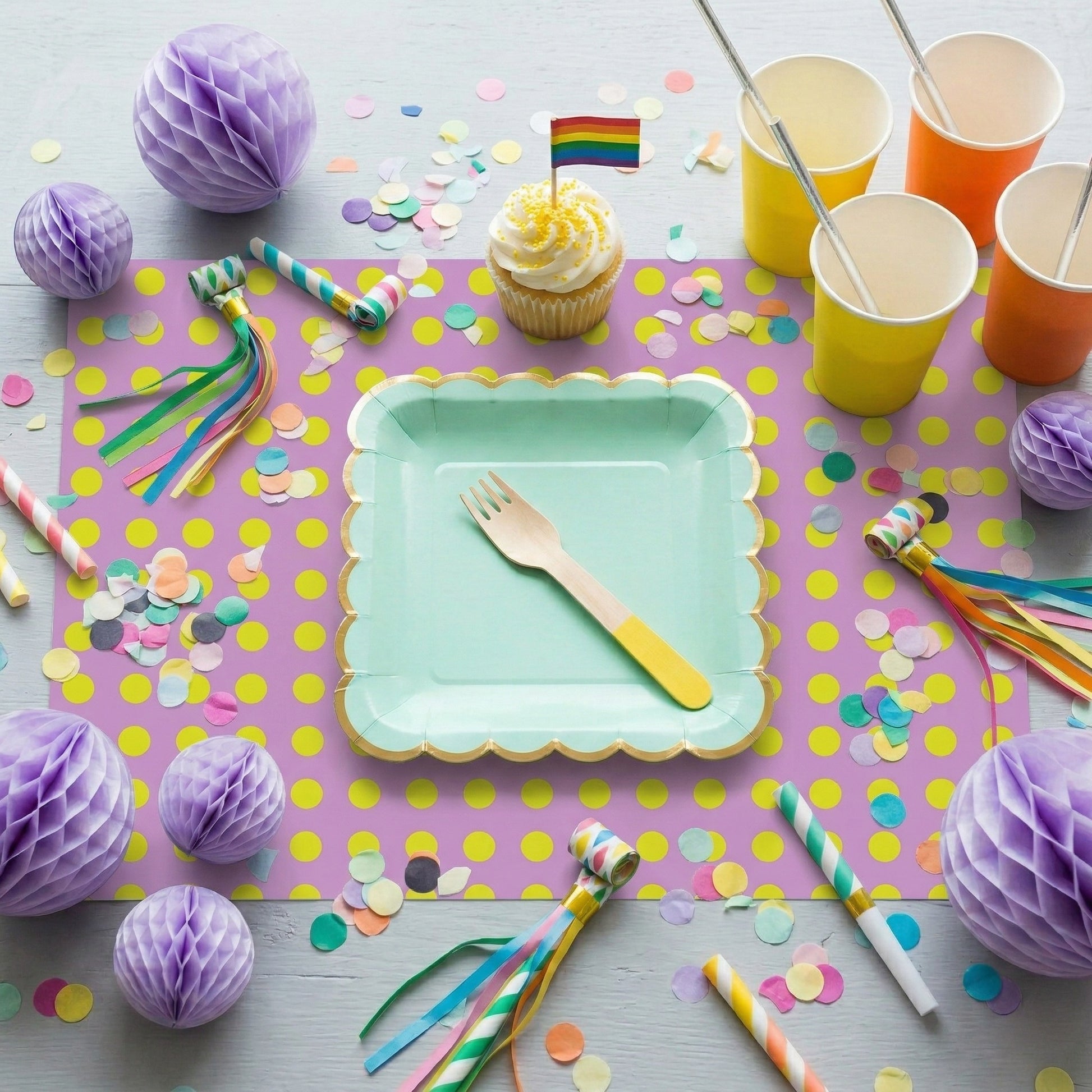 Party setup with colorful plates, cups, and decorations on a polka dot paper placemat.