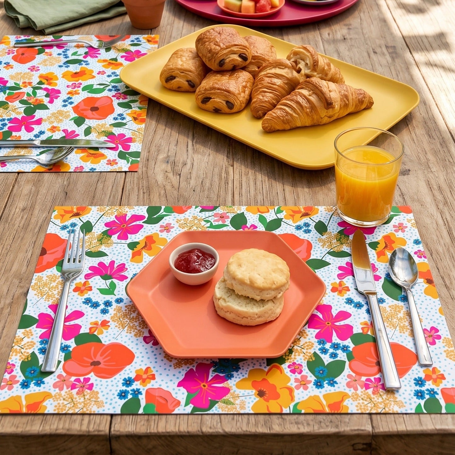 Outdoor table setting with colorful paper placemats, food, and drinks on a wooden table.