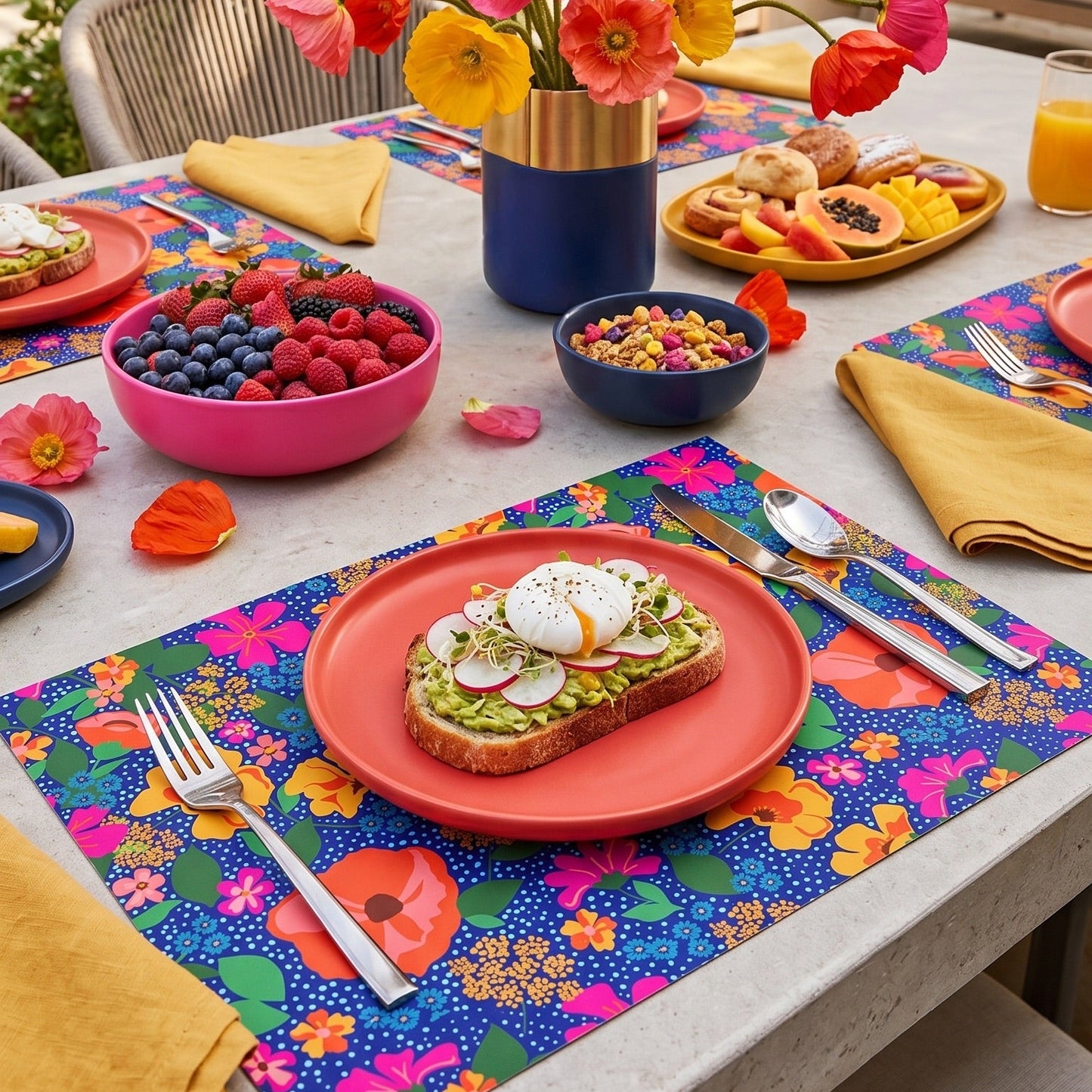 Outdoor table setting with colorful floral centerpiece, plates of food, and floral paper placemats.