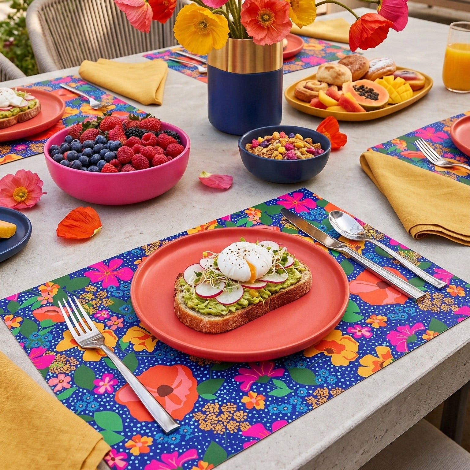 Outdoor table setting with colorful floral centerpiece, plates of food, and floral paper placemats.