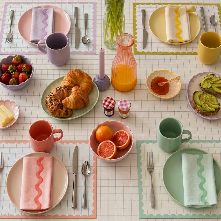 Dining table set with colorful plates, cups, and utensils on paper placemats.