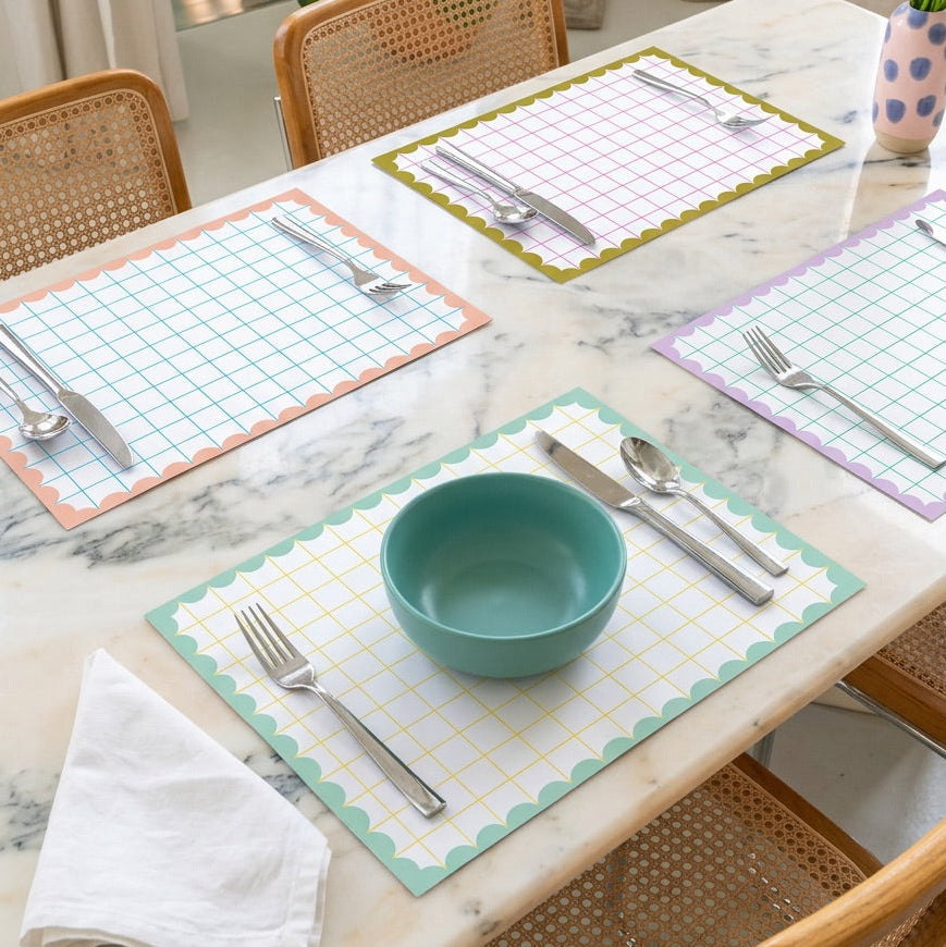 Dining table set with grid scallop paper placemats, bowls, and cutlery on a marble surface.