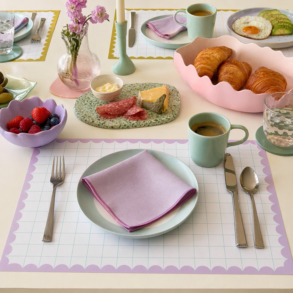Breakfast table setting with pastel colors, including croissants, coffee, and colorful paper placemats.
