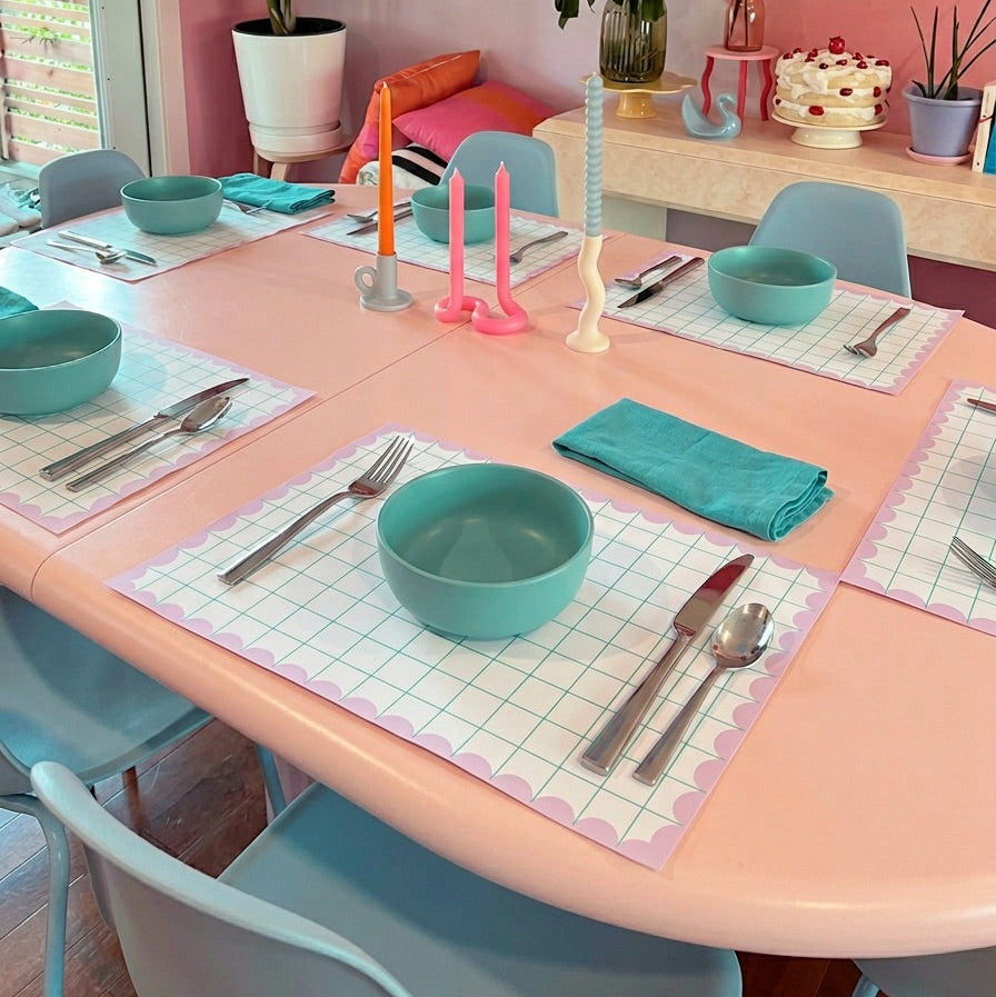 Colorful dining setup with pink table, blue chairs, and turquoise bowls and grid paper placemats.