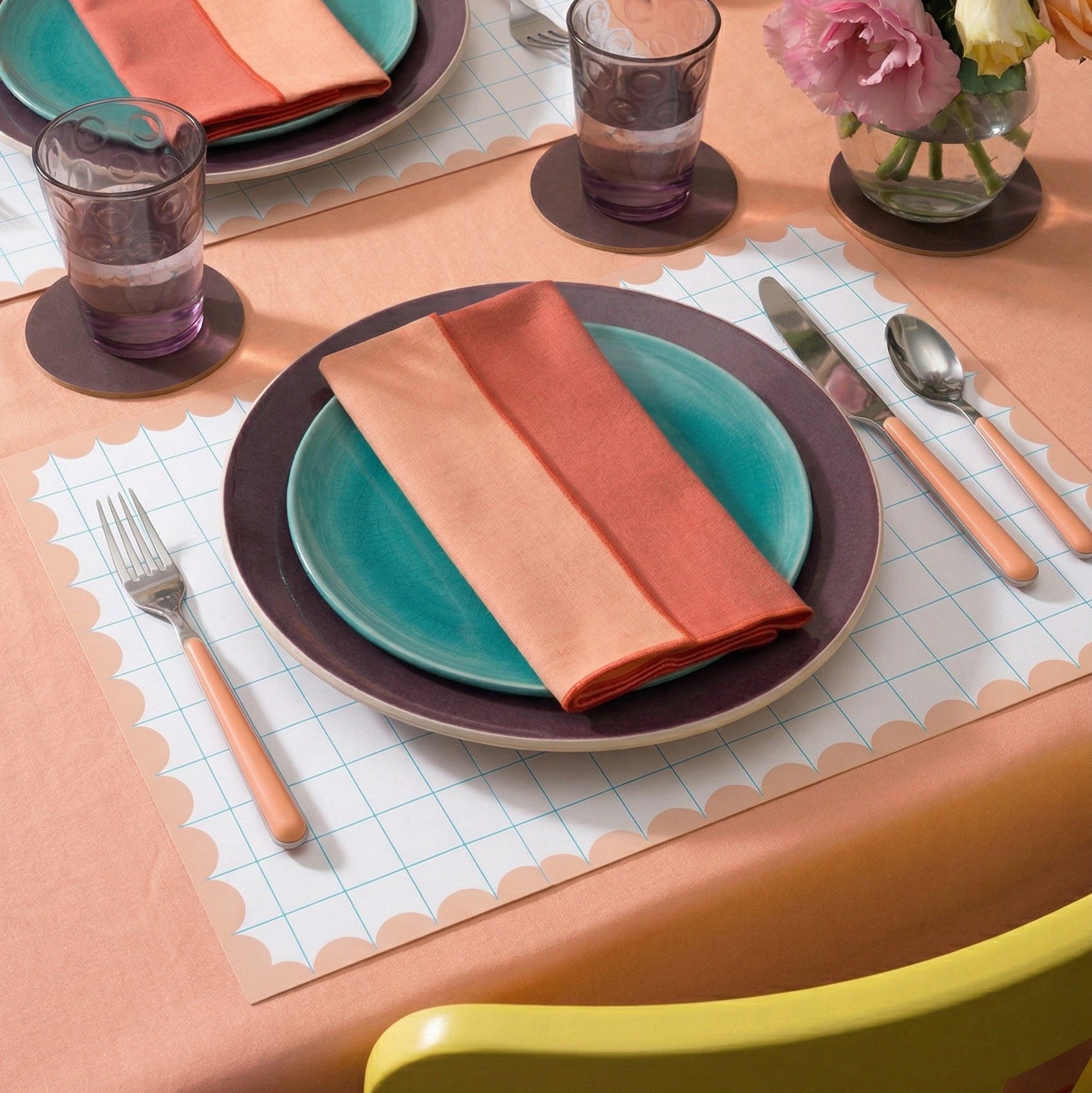 Dining table setting with colorful plates, napkins, and grid paper placemats.