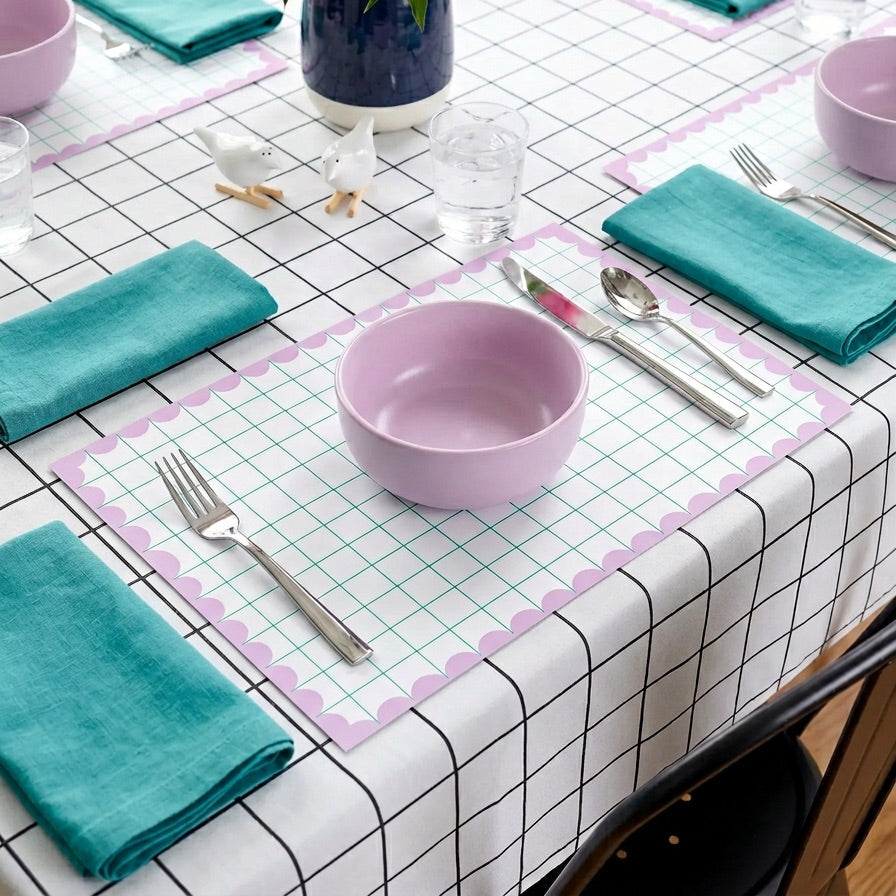 Dining table setting with pink and turquoise place settings, flowers, and grid-patterned placemats.
