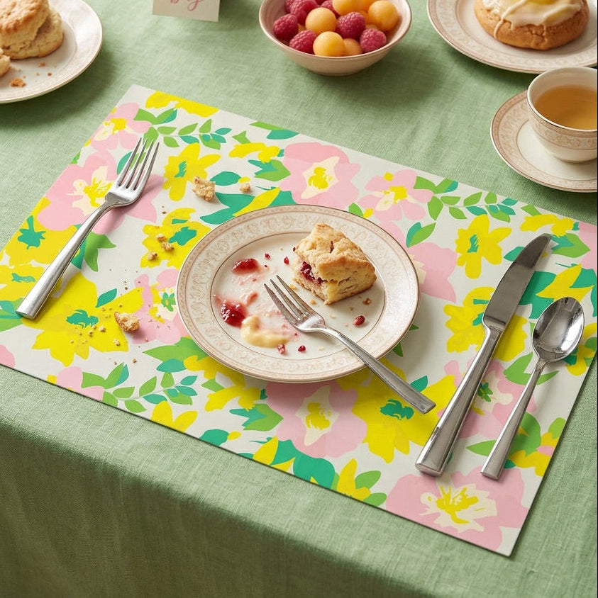 Table setting with floral paper placemats, plates with food, and cutlery on a green tablecloth.