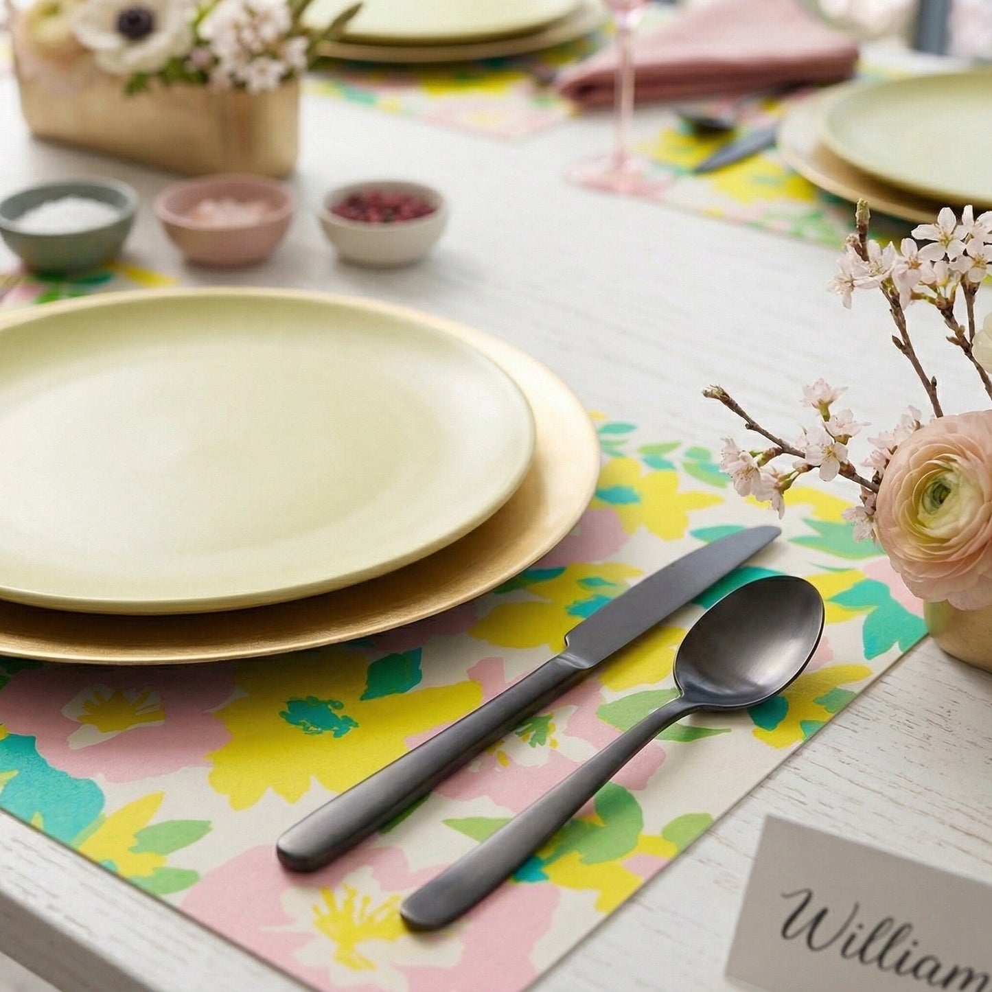 Dining table setting with plates, cutlery, and floral decorations on a floral paper placemat.