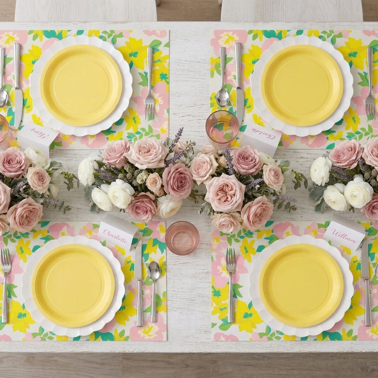 Set dining table with yellow plates, floral paper placemats, and pink napkins.