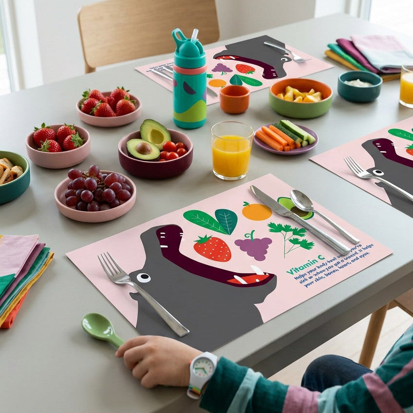 Children's table setting with colorful placemats, plates of food, and a child's hand reaching out.